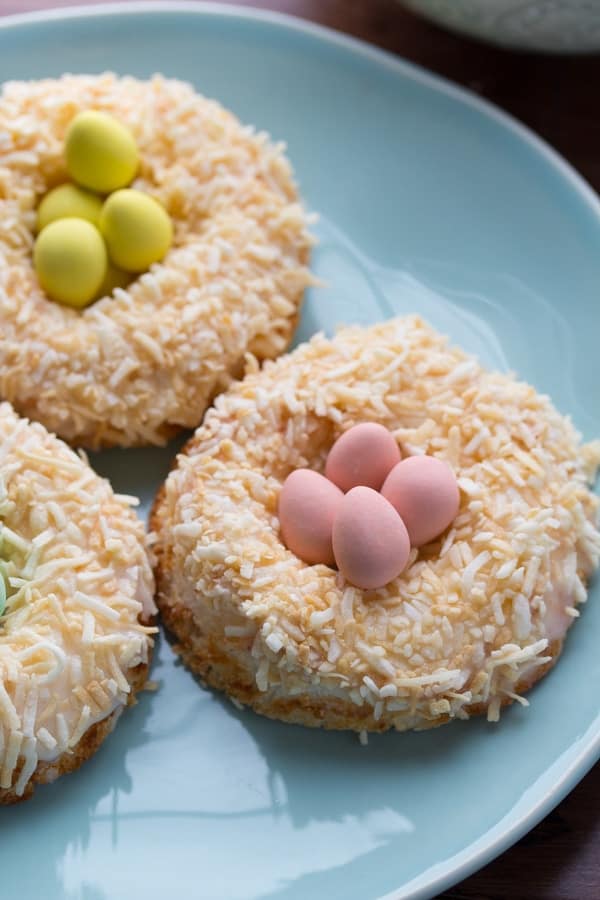 3 lemon angel food cake donuts with coconut topping and easter eggs in the middle on blue plate