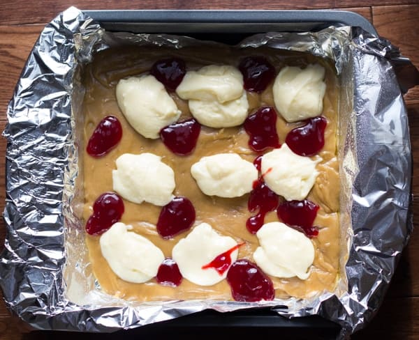 overhead view of raw blondie batter in pan with dollops of cream cheese and raspberry jam