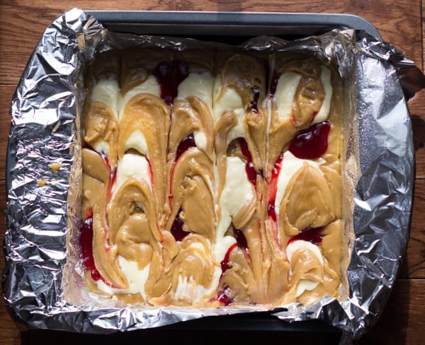 overhead view of raw blondie batter in pan with dollops of cream cheese and raspberry jam swirled together