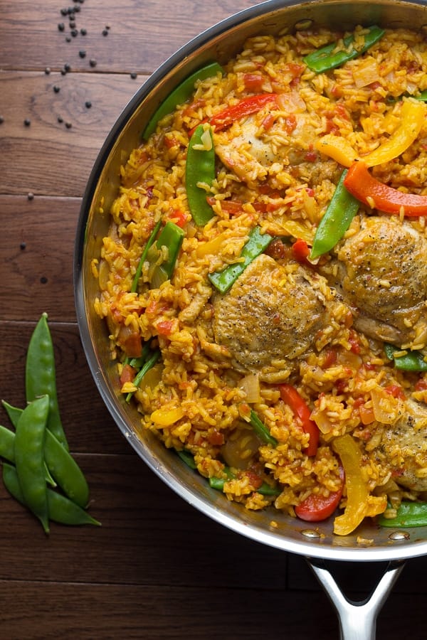 Spanish Chicken and Rice Skillet in a large pan with fresh snap peas on the side