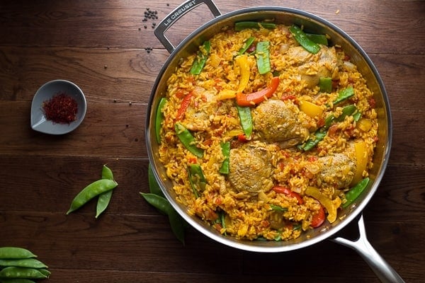 Overhead view of Spanish Chicken and Rice Skillet with snap peas and saffron threads on the side