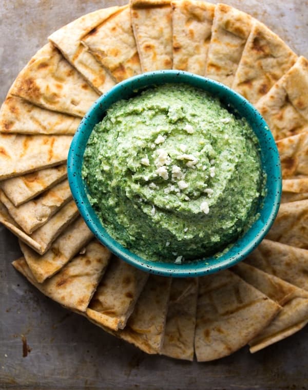 overhead view of a bowl of spinach artichoke whipped feta with pita chips surrounding it