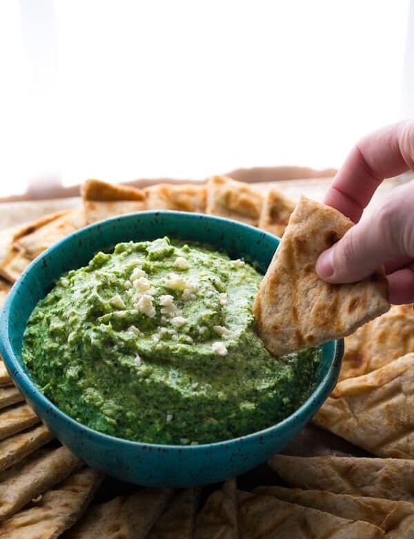 hand dipping pita into spinach artichoke feta dip
