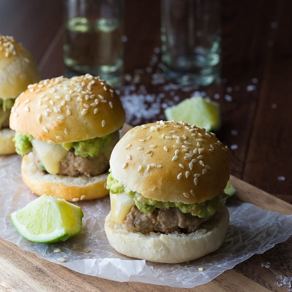 two tequila turkey sliders on cutting board with shots of tequila in the background