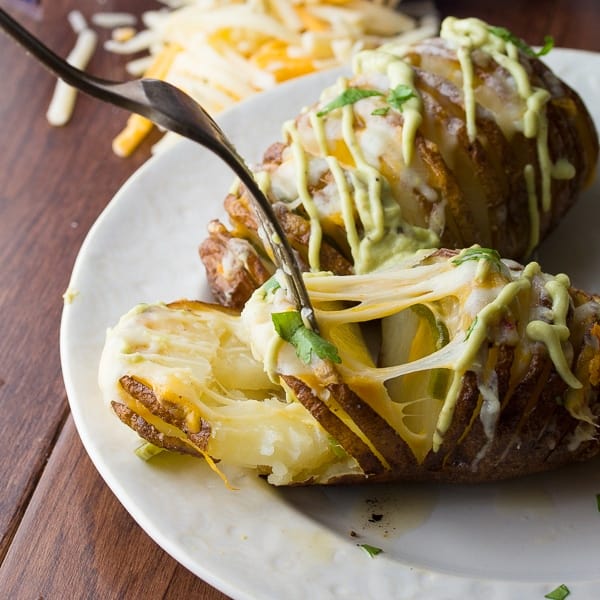 fork prying apart the layers of a hasselback potato revealing melted cheese and jalapenos