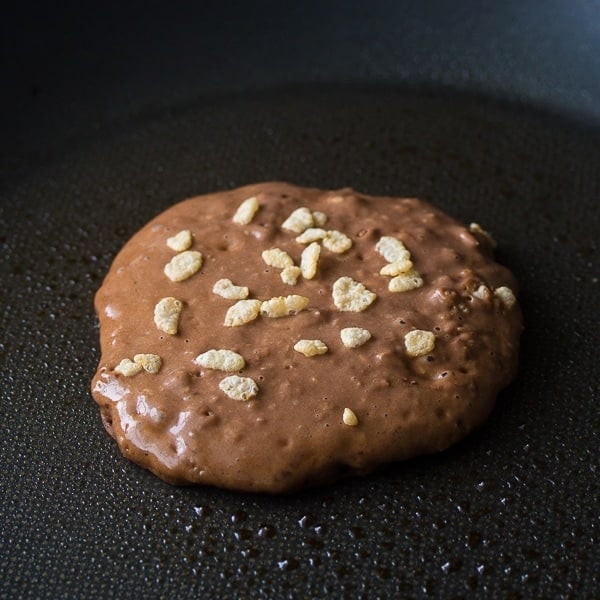 showing how to sprinkle the chocolate pancake with rice krispies while cooking