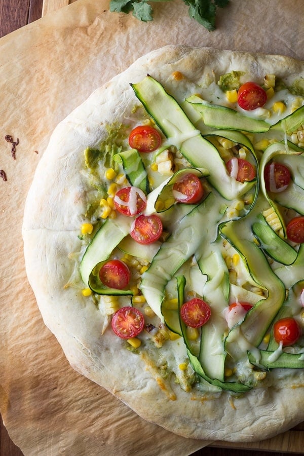 fully baked guacamole pizza with all toppings: corn, zucchini and cherry tomatoes