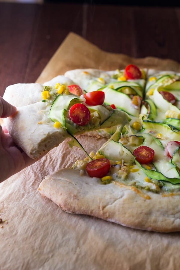 hand grabbing a slice of guacamole pizza off parchment paper