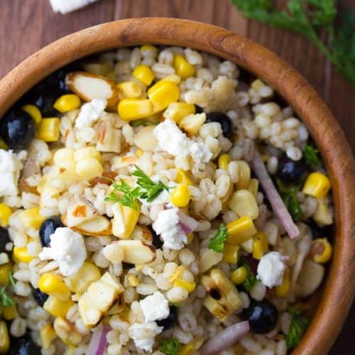 overhead view of Summer barley salad with corn and blueberries in wooden bowl