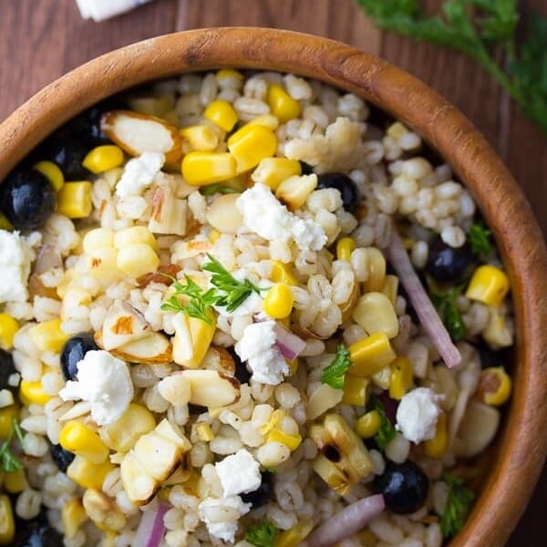 overhead view of Summer barley salad with corn and blueberries in wooden bowl