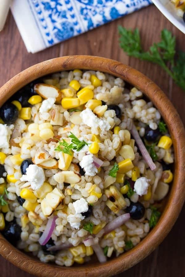 overhead view of Summer barley salad with corn and blueberries in wooden bowl