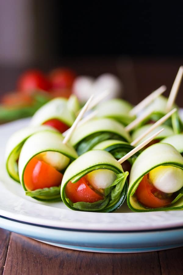 Rows of zucchini roll ups on ap late with tomatoes, basil, and mozzarella 