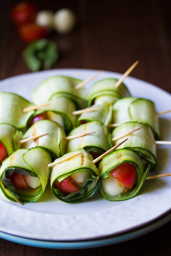 zucchini roll ups on a white plate with tomatoes, basil, and mozzarella after grilling
