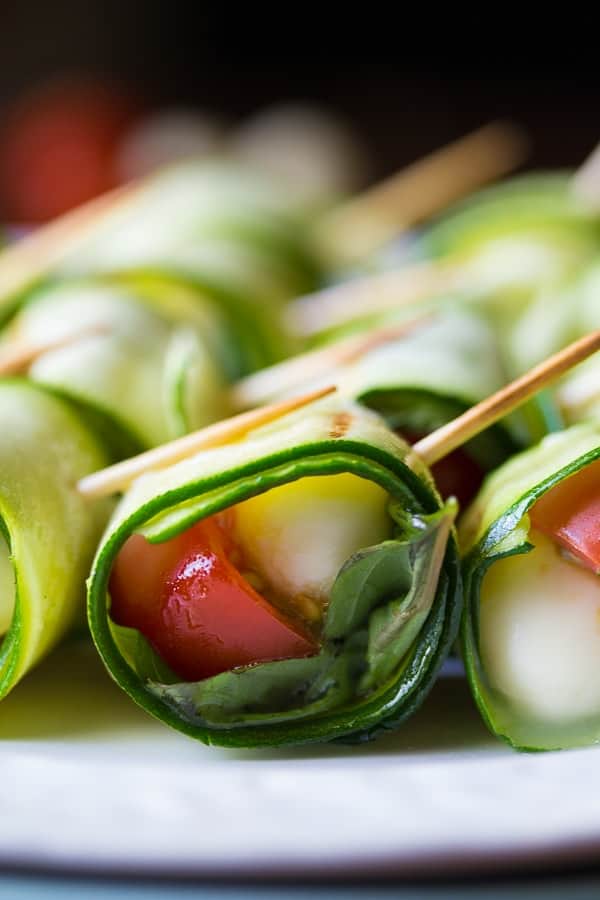 Side view of grilled caprese zucchini roll ups on a plate