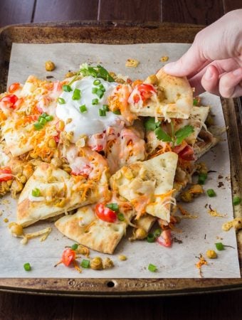 A hand picking up a spiced chickpea naan nacho from pile of nachos