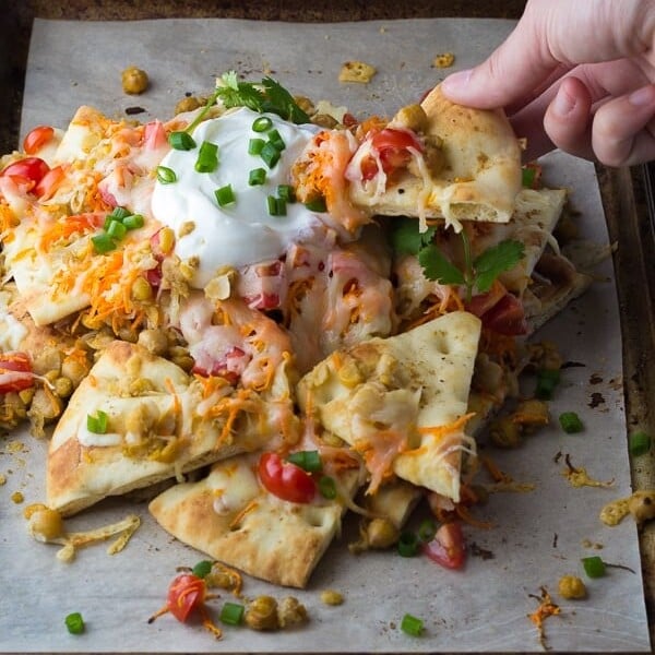 hand picking up a spiced chickpea naan nacho from pile of nachos