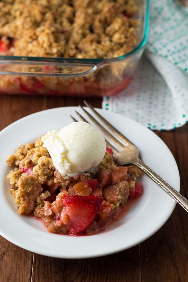 side angle view of strawberry rhubarb crisp on plate with a scoop of ice cream and a fork