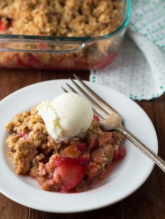strawberry rhubarb crisp with oatmeal cookie streusel in white bowl with ice cream scoop and fork