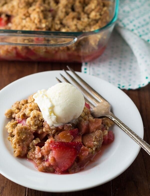 strawberry rhubarb crisp with oatmeal cookie streusel in white bowl with ice cream scoop and fork