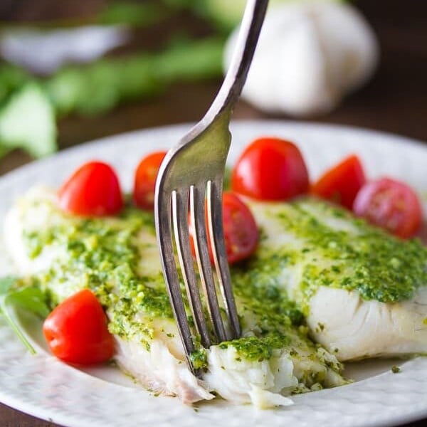 cilantro chile pesto fish on white plate with tomatoes and fork