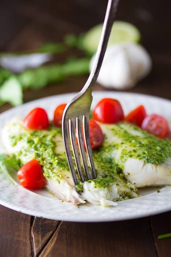 cilantro chile pesto fish on white plate with tomatoes and fork