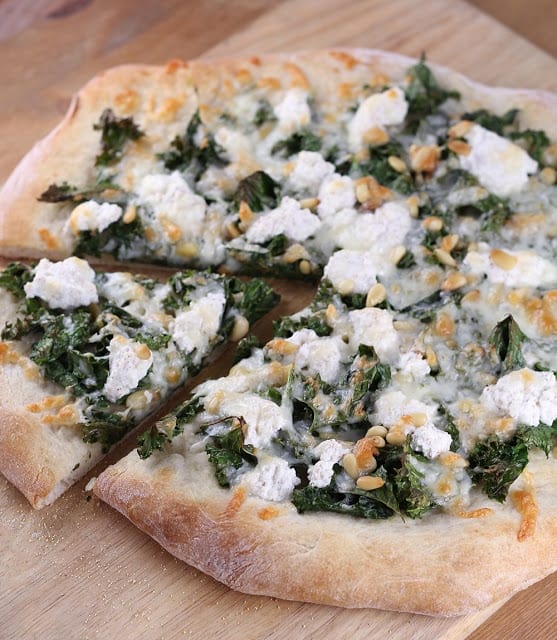 kale pine nut and ricotta pizza on cutting board with a slice cut out