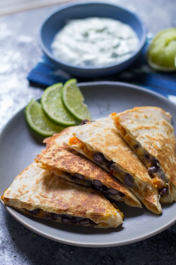 sweet potato black bean quesadillas on a plate with lime wedges and a bowl of yogurt in the background