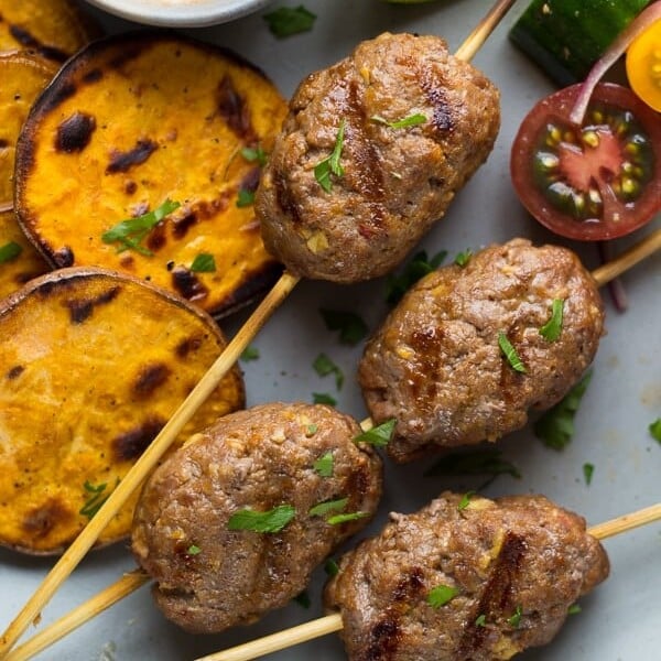 thai curry beef koftas with coconut sauce on gray plate with sweet potatoes and tomatoes