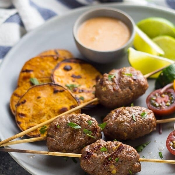 thai curry beef koftas with coconut sauce on gray plate with sweet potatoes and tomatoes and lime wedges