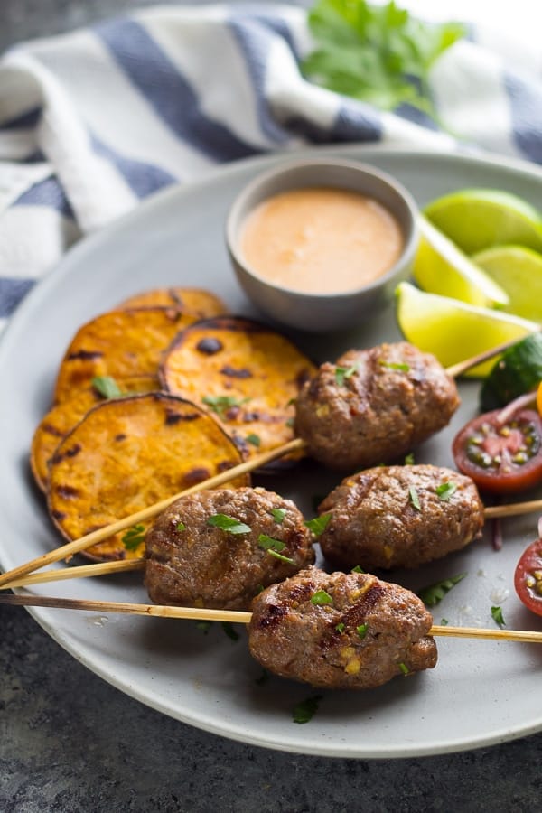 side angle view of thai beef koftas on plate with sweet potatoes, limes and coconut dipping sauce