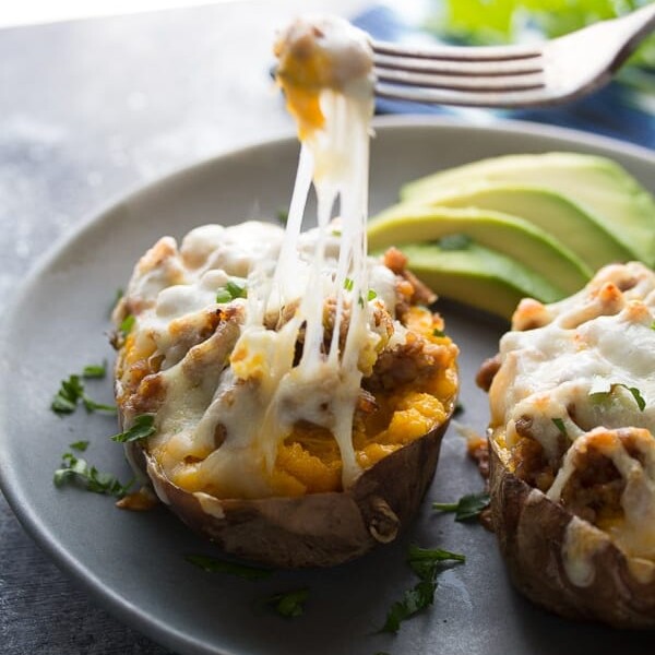 baked sweet potatoes with sausage and pepperjack on gray plate with avocado slices and fork