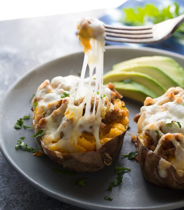 baked sweet potatoes with sausage and pepperjack on gray plate with avocado slices and fork