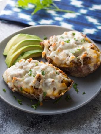 two baked sweet potatoes with sausage and pepperjack on gray plate with avocado slices