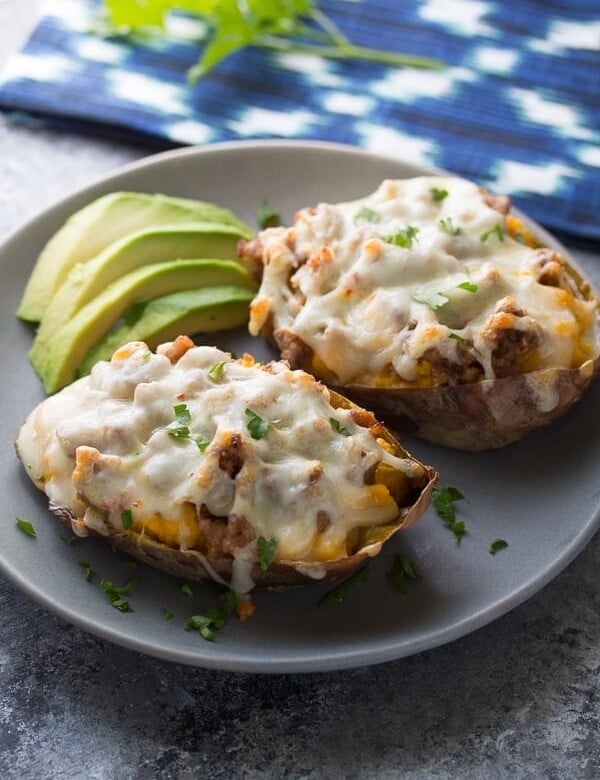 two baked sweet potatoes with sausage and pepperjack on gray plate with avocado slices
