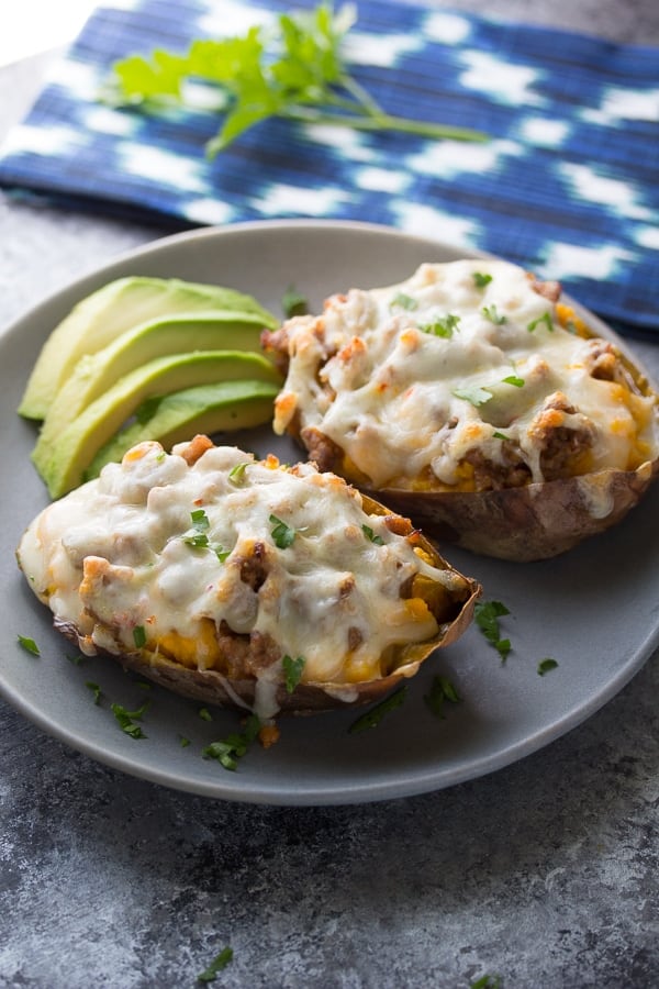 two sausage-stuffed sweet potatoes on a plate with avocado 