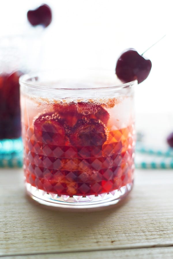 side angle view of a glass filled with cherry bourbon cocktail with a fresh cherry on the glass side