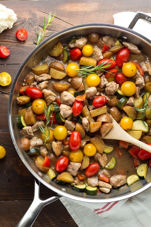 overhead view of skillet containing chicken, potatoes, herbs and tomatoes