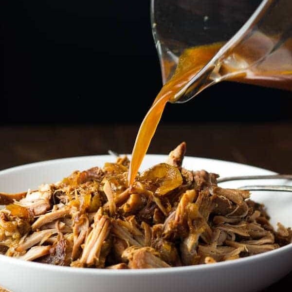 slow cooker maple pulled pork in white bowl with sauce being poured over
