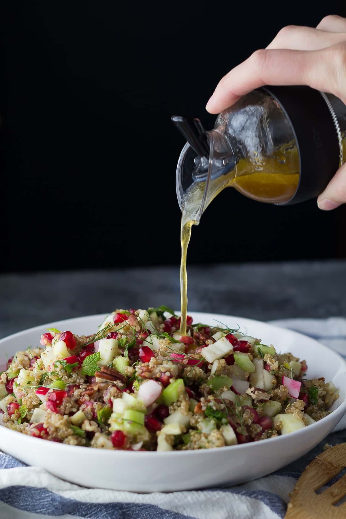 pouring vinaigrette over a bowl holding the fennel quinoa salad