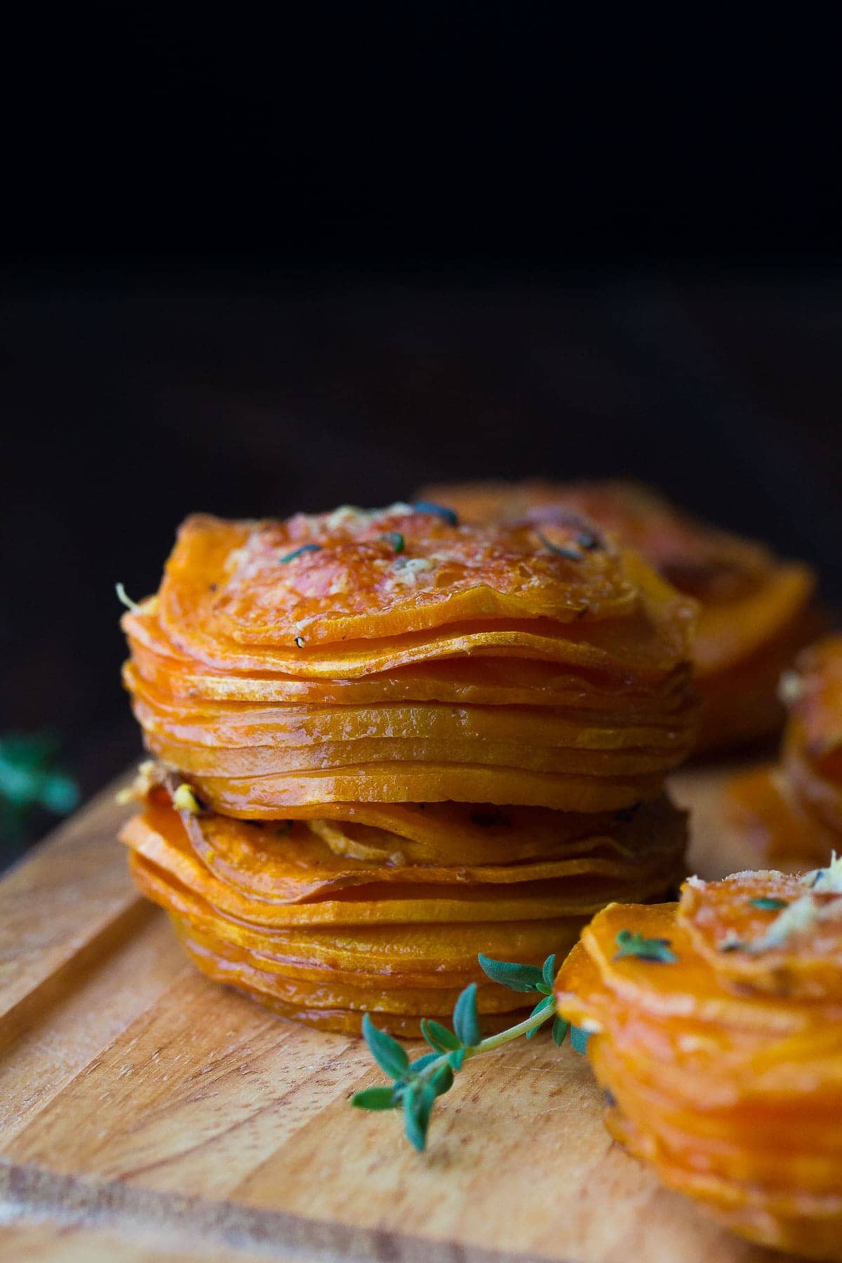 side view of sweet potato stacks on cutting board with fresh herbs