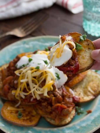 chili potato nachos on blue plate with hand taking one