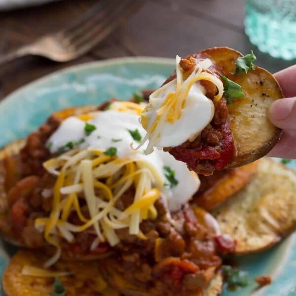 chili potato nachos on blue plate with hand taking one