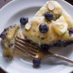 overhead shot of deep dish blueberry almond pancake on white plate with fork