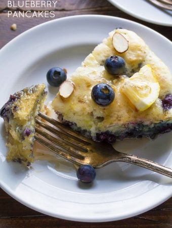 overhead shot of deep dish blueberry almond pancake on white plate with fork