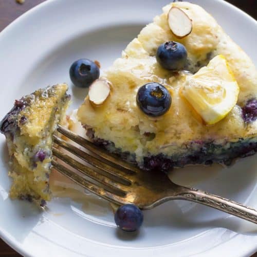 overhead shot of deep dish blueberry almond pancake on white plate with fork