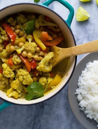 chickpea and cauliflower curry in bowl with wood spoon and rice