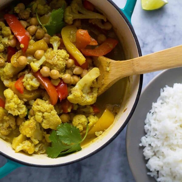 chickpea and cauliflower curry in bowl with wood spoon and rice