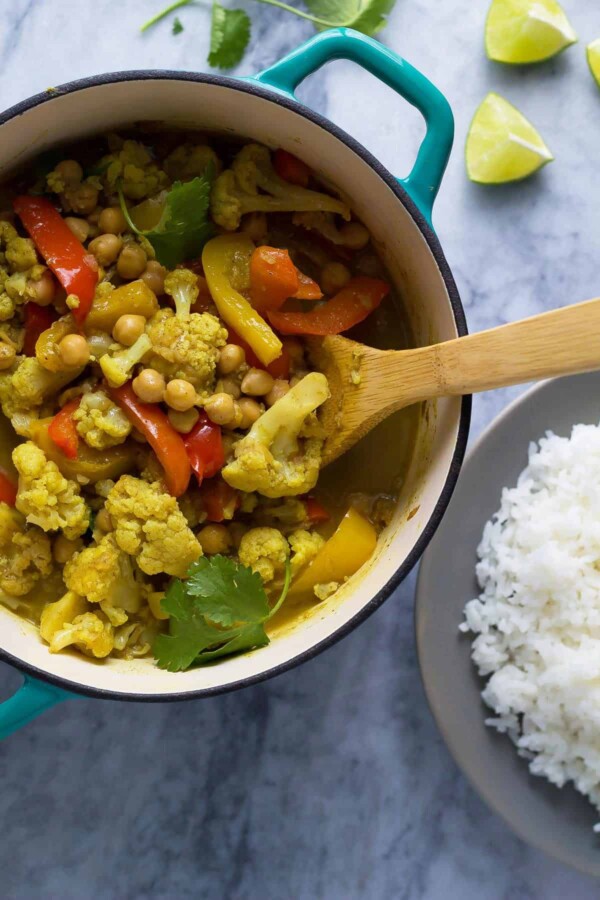 chickpea and cauliflower curry in bowl with wood spoon and rice