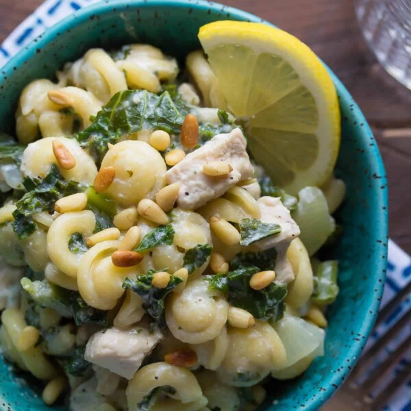 overhead shot of pasta with kale and goat cheese in blue bowl with lemon slice