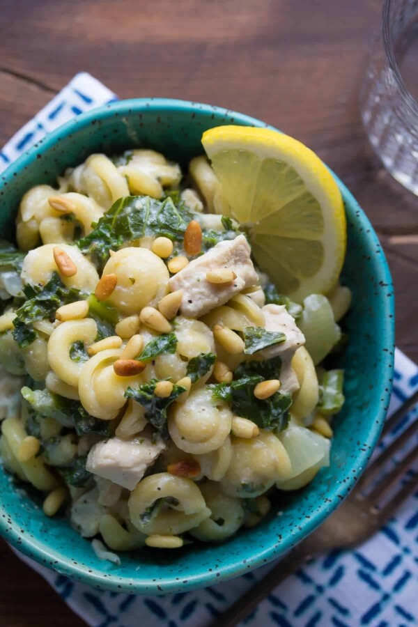 overhead shot of pasta with kale and goat cheese in blue bowl with lemon slice